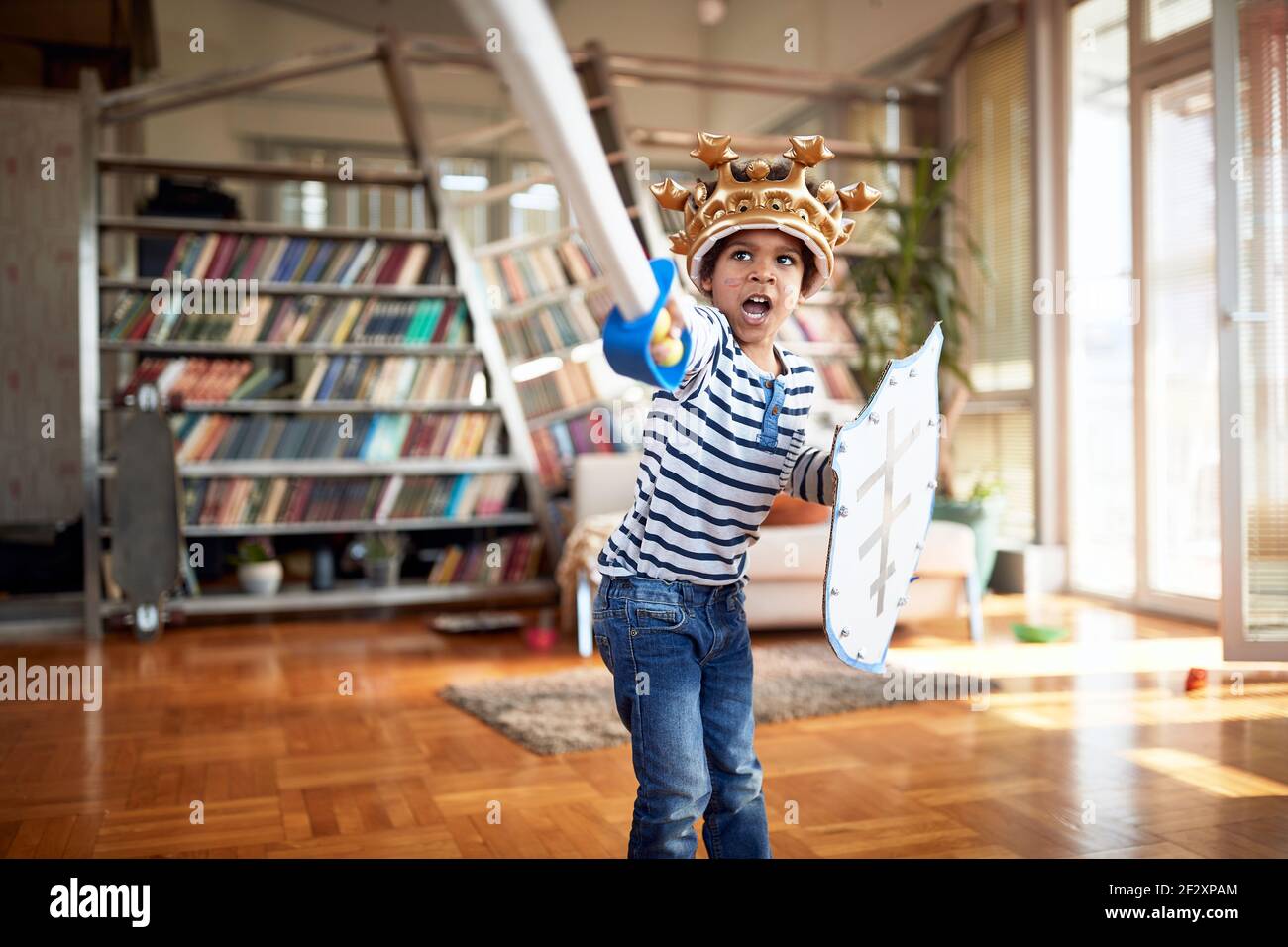 Un petit garçon mignon avec une épée et un bouclier qui crie et attaque tout en jouant dans une atmosphère ludique à la maison. Famille, ensemble, amour, temps de jeu Banque D'Images