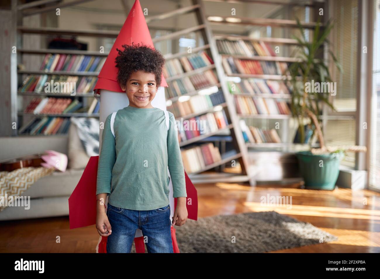 Un petit garçon avec un jouet de fusée sur son dos pose en jouant dans une atmosphère détendue à la maison. Maison, jeu, enfance Banque D'Images