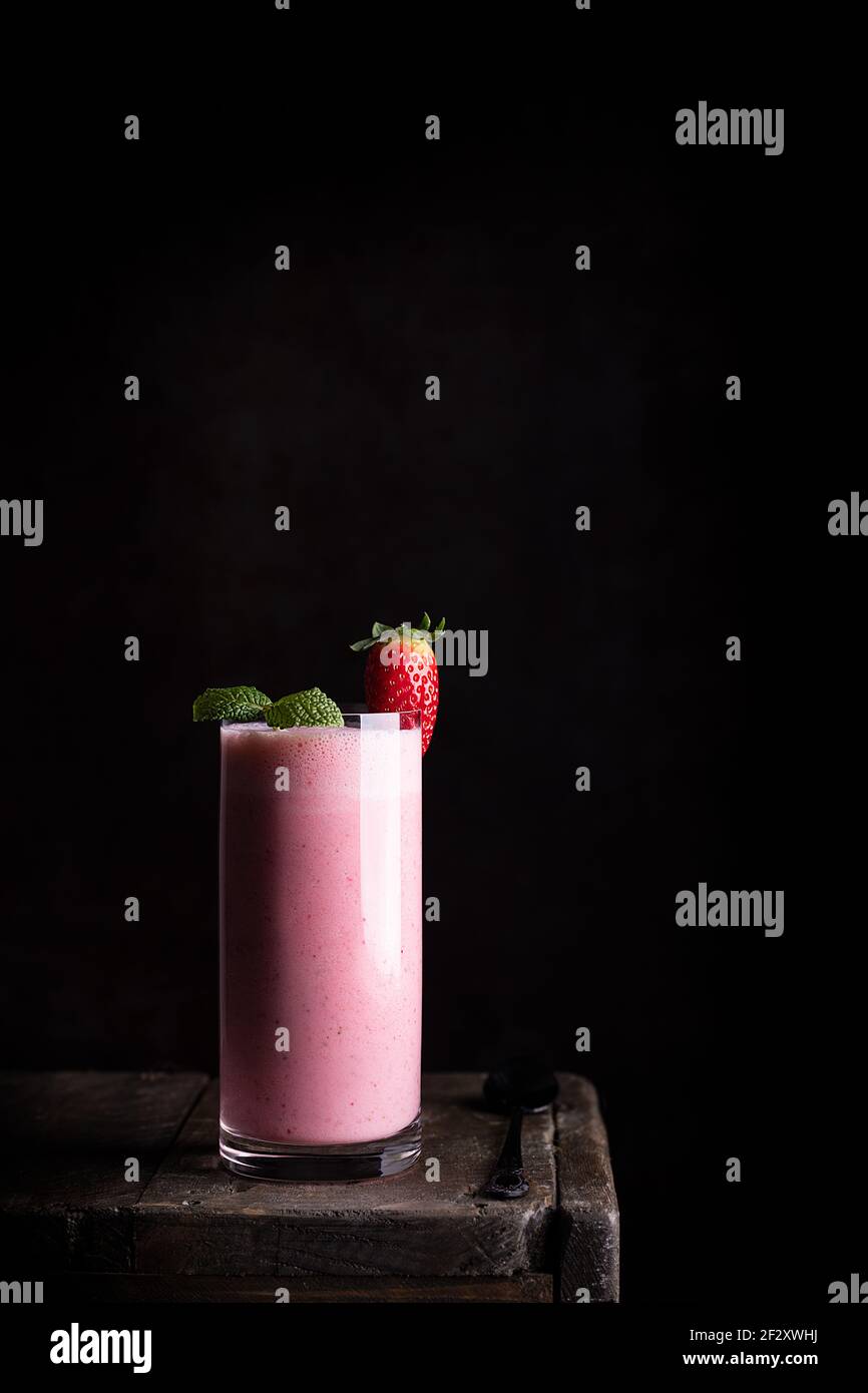 Délicieux milk-shake maison sain avec des fraises fraîches garnies de vert feuilles de menthe servies en verre sur une table en bois contre le noir arrière-plan Banque D'Images