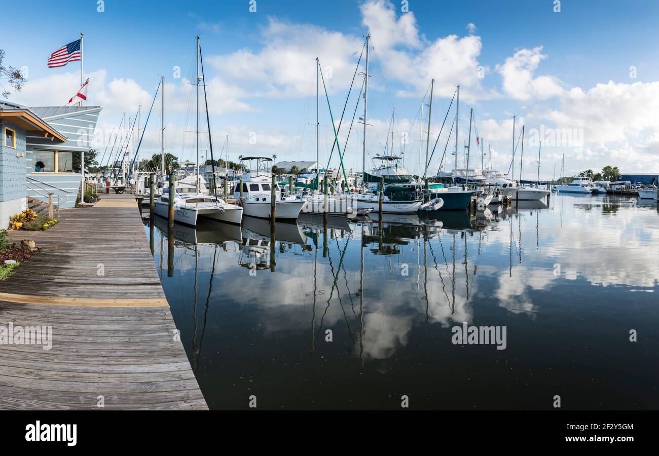 Plusieurs bateaux de voile et de pêche amarrés dans une marina avec ciel bleu et nuages blancs reflétés sur l'eau miroir, New Smyrna Beach, Floride, États-Unis. Banque D'Images