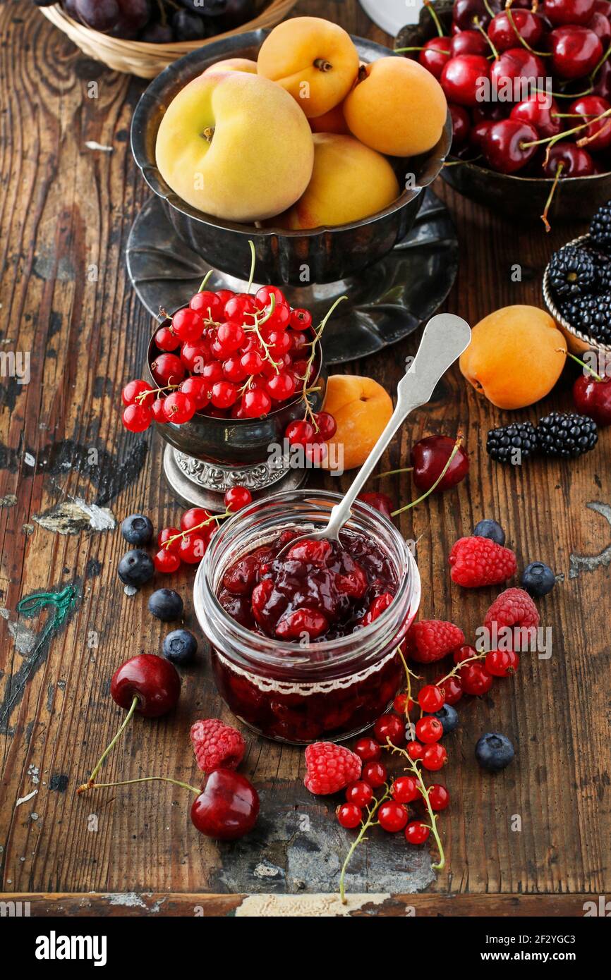 Pots de confiture de fraises de cerise parmi les fruits d'été et d'automne sur une table en bois. Banque D'Images