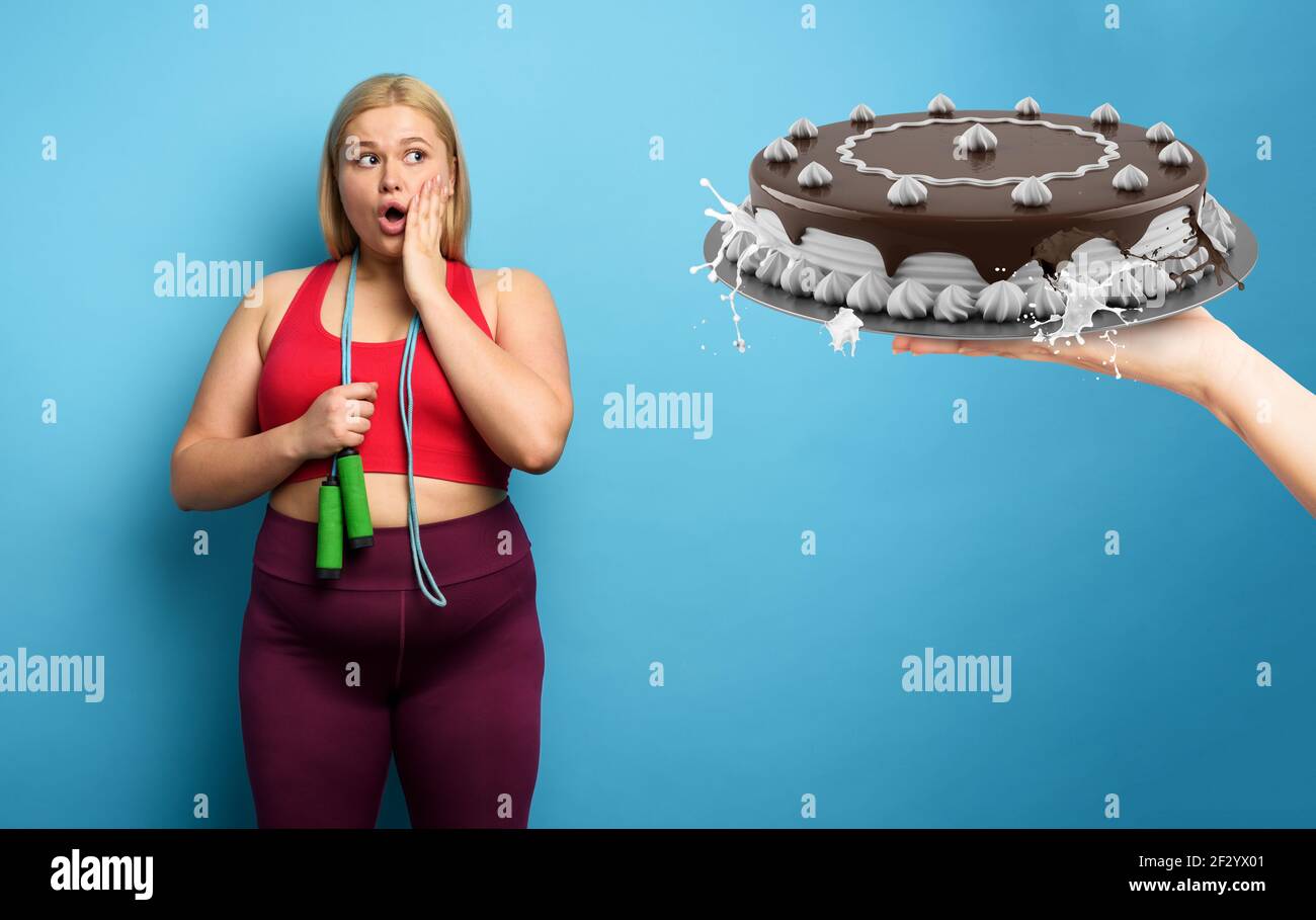 FAT girl fait de la gym mais elle veut manger un grand gâteau. Fond cyan Banque D'Images