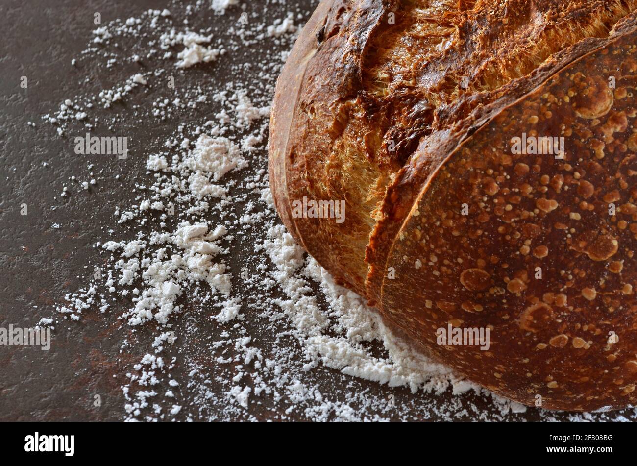 Gros plan de pain maison avec une croûte croustillante sur le table de cuisine arrosée de farine Banque D'Images
