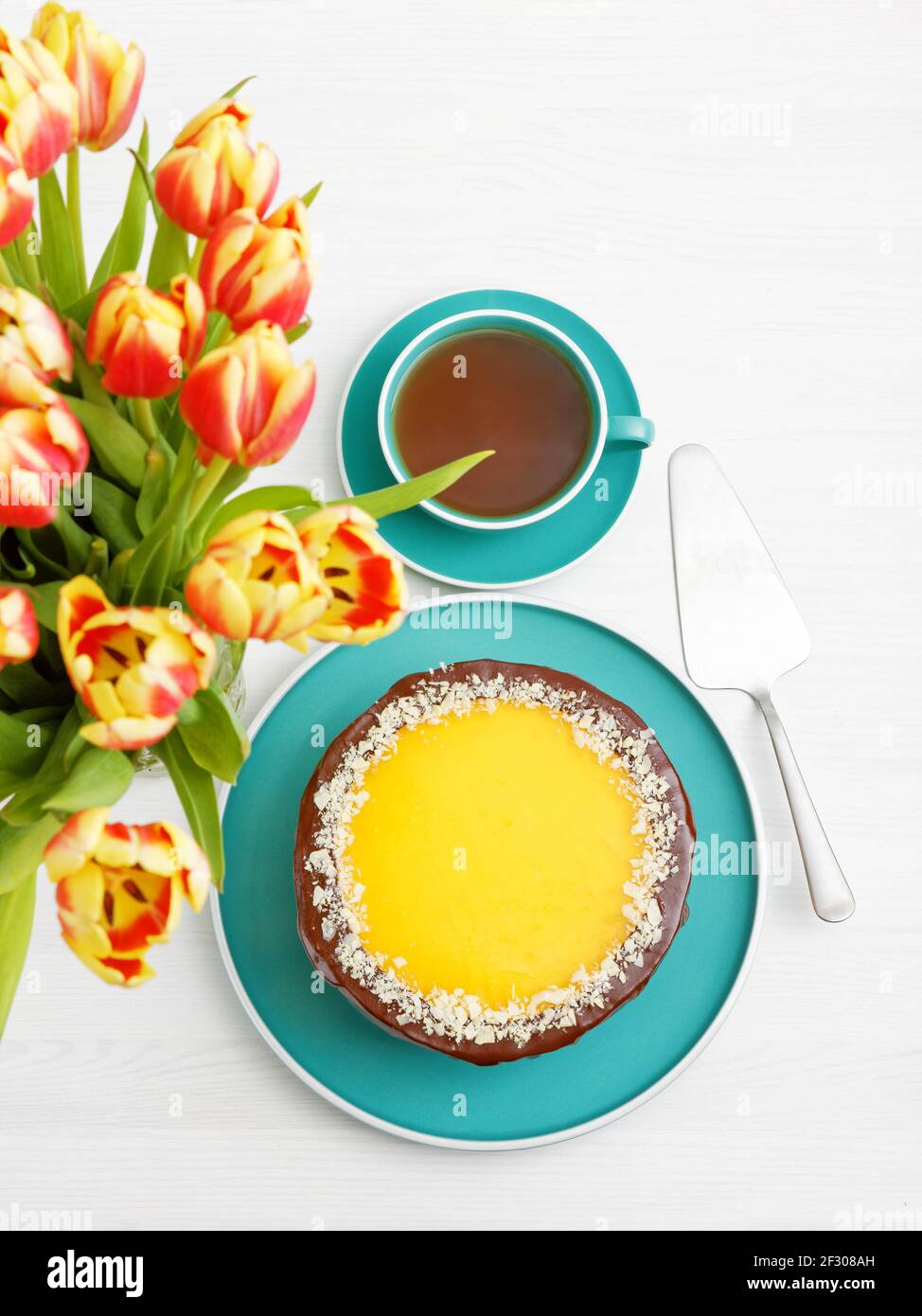 Gâteau au chocolat et à l'orange maison parsemé de tranches d'amande et d'une tasse de thé sur une table en bois blanc. Vue de dessus. Journée internationale de la femme. Banque D'Images Gâteau au chocolat et à l'orange maison parsemé de tranches d'amande et d'une tasse de thé sur une table en bois blanc. Vue de dessus. Journée internationale de la femme. Banque D'Images