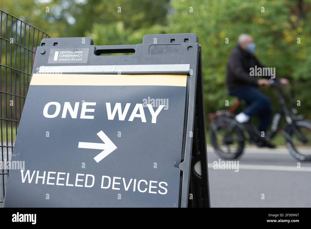 Cycliste flou et panneau dans Central Park: Aller simple Banque D'Images