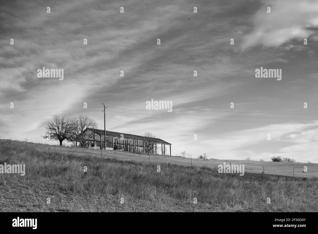 Une ferme abandonnée avec ciel nuageux derrière en noir et blanc avec arbres sans feuilles Banque D'Images