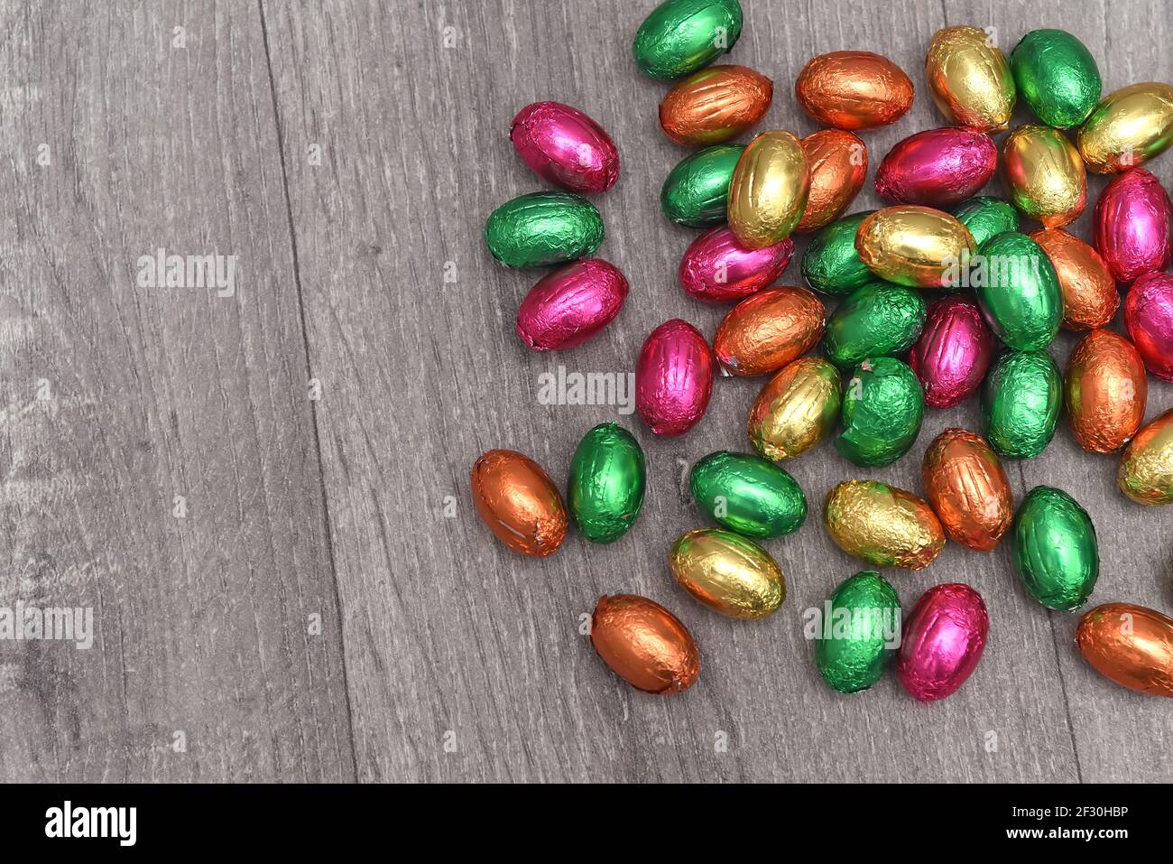 Feuilles enveloppées d'oeufs de pâques multicolores dans le rose, le vert, l'orange et le jaune dans une pile ou un groupe, sur un fond de bois gris blanc. Banque D'Images