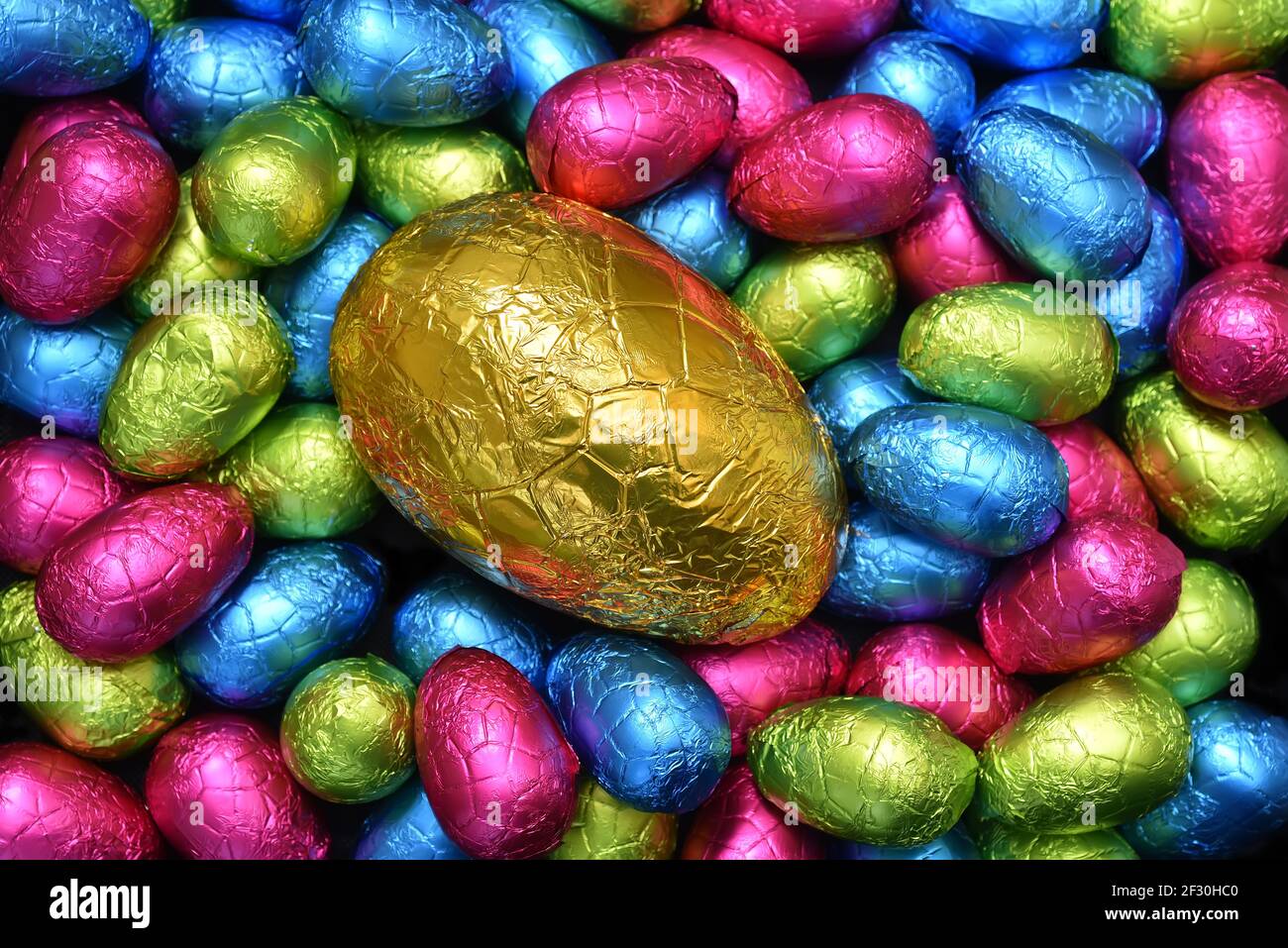 Pile ou groupe de plusieurs couleurs et différentes tailles d'oeufs de pâques au chocolat enveloppés d'une feuille colorée en rose, bleu, jaune et vert lime. Banque D'Images