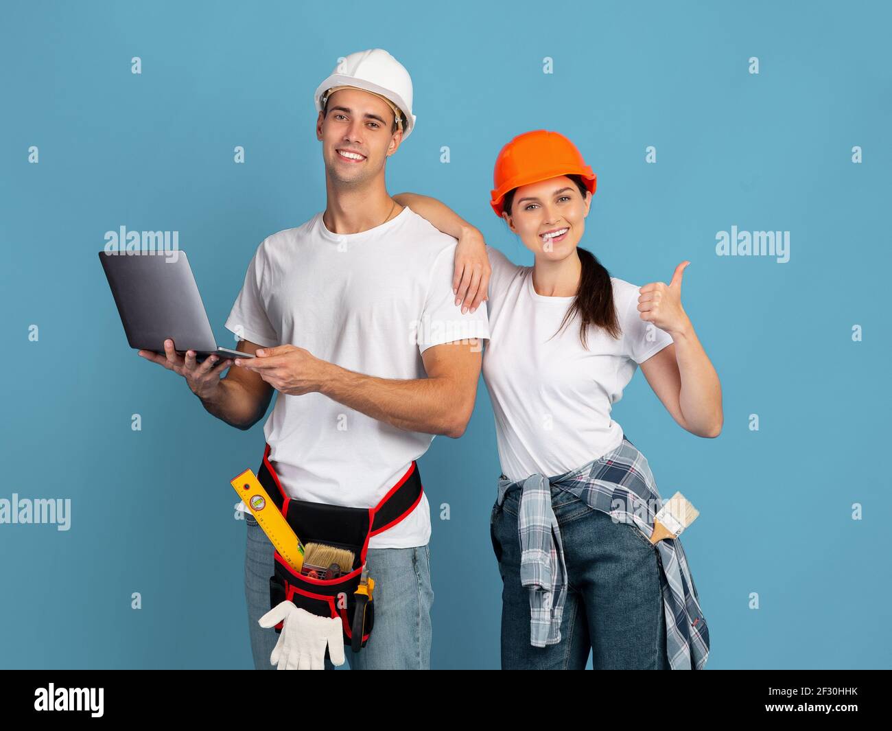 Achat en ligne pour réparation. Couple en casque de sécurité tenant un ordinateur portable montrant le pouce vers le haut Banque D'Images