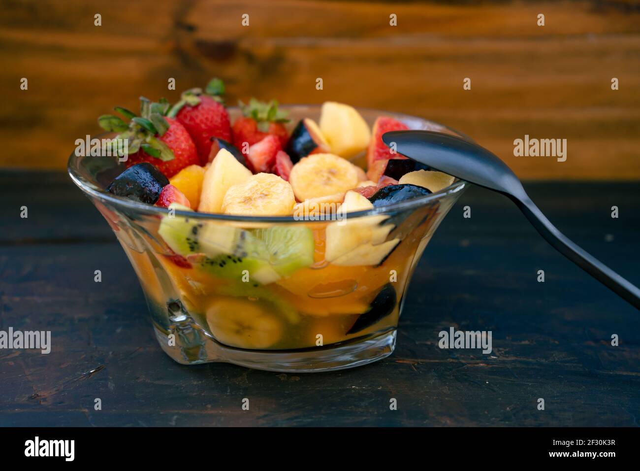 Salade de fruits naturelle et saine à l'orange dans un bol en verre transparent, sur une surface noire rustique. Concept d'alimentation saine, vie saine. 45 degrés Banque D'Images