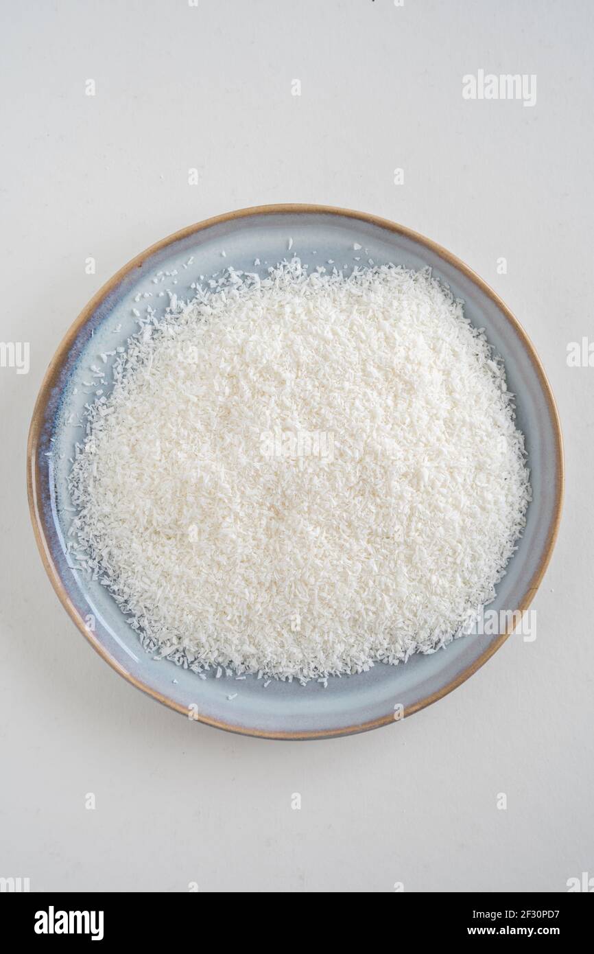 Vue d'oiseau d'une assiette bleue avec noix de coco déshydratée sur fond blanc, rasage de noix de coco séchées, avec espace de copie Banque D'Images