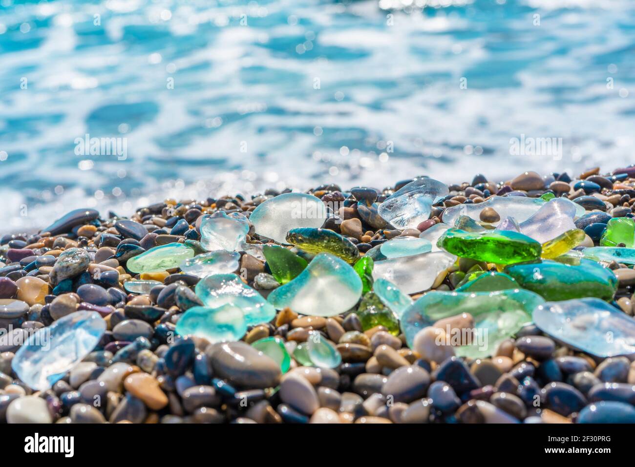 Verre de mer texturé à polir naturel et pierres sur le bord de mer. Eau de  mer claire d'azur avec vagues. Verre vert, bleu brillant avec cailloux de  mer multicolores Photo Stock -