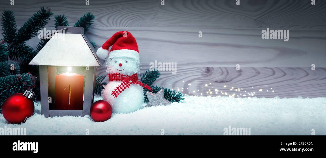 Premier Avent. Lanterne de Noël et bonhomme de neige avec chapeau du père noël sur neige blanche. Banque D'Images