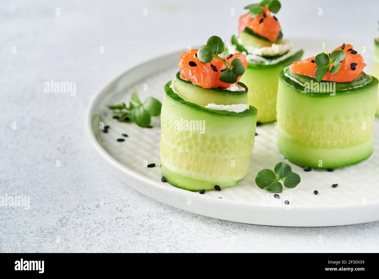 Petits pains aux concombres au fromage doux, morceaux de saumon salé, microverts et sésame noir servis sur une assiette blanche. Hors-d'œuvre de légumes des fêtes. Sélection Banque D'Images