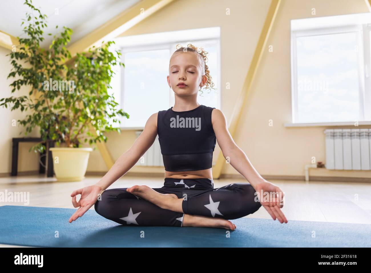 Une petite fille de vêtements de sport, pratiquant le yoga, est engagée dans la méditation assise dans la position lotus dans la salle. Concept de yoga pour enfants. Banque D'Images