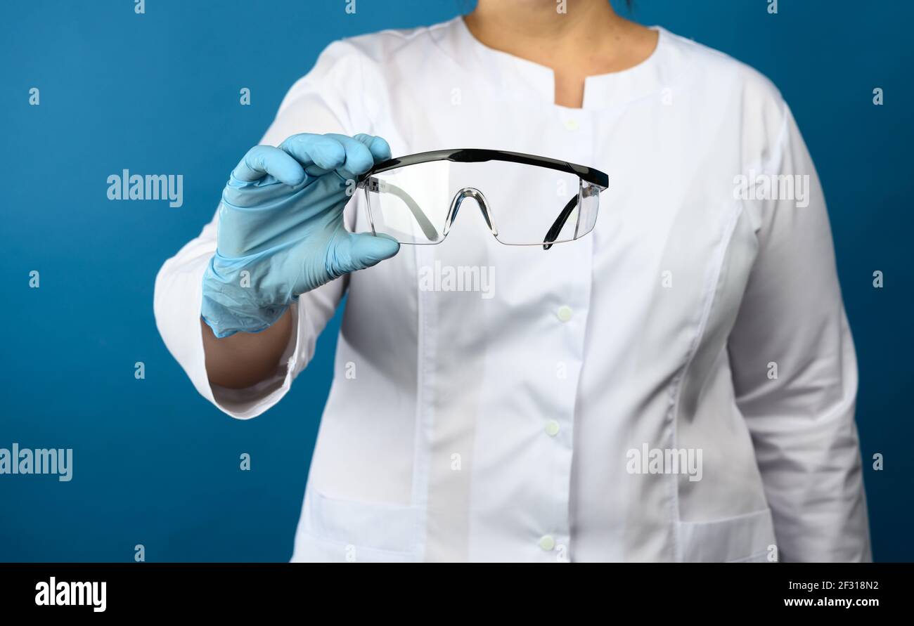 Femme médecin dans une robe médicale blanche se tient sur un fond bleu et contient des lunettes de protection en plastique Banque D'Images