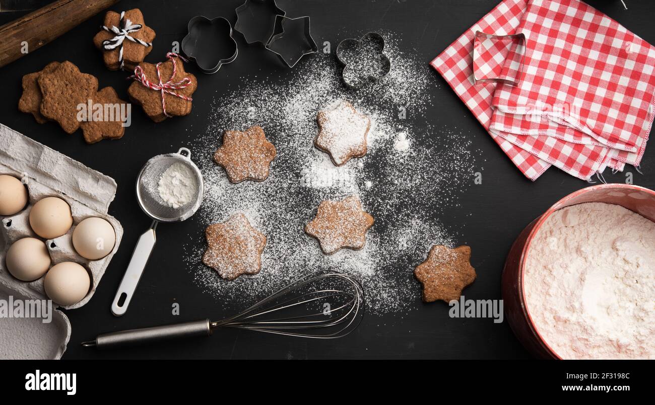 Biscuit au pain d'épice cuit en forme d'étoile arrosé de sucre en poudre sur un table noire et ingrédients Banque D'Images