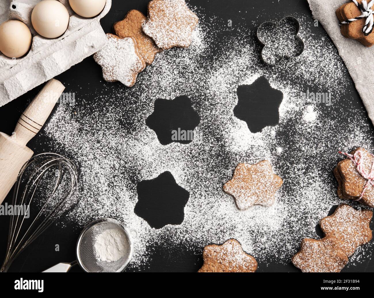 Biscuit au pain d'épice cuit en forme d'étoile arrosé de sucre en poudre sur un table noire et ingrédients Banque D'Images