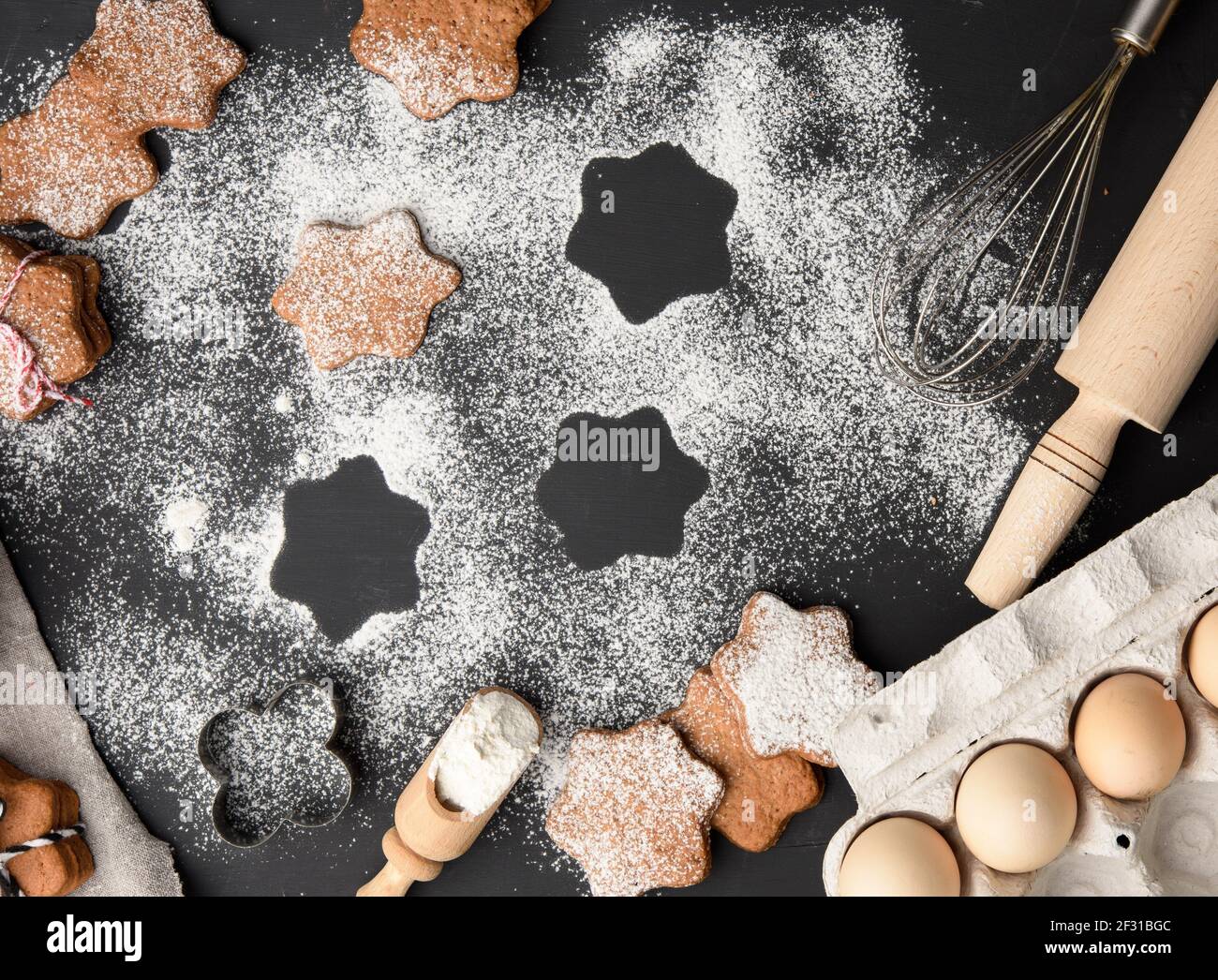 Biscuit au pain d'épice cuit en forme d'étoile arrosé de sucre en poudre sur un table noire et ingrédients Banque D'Images