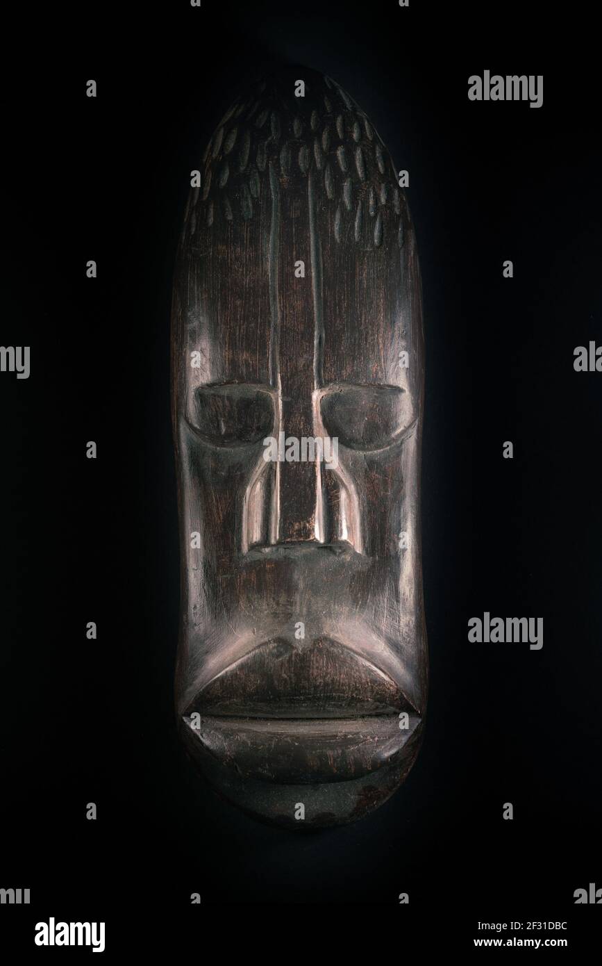 Sculpture en bois de visage humain de style africain. Sculpture en bois sombre. Masque tribal africain isolé sur fond noir. Art et culture de l'Afrique Banque D'Images