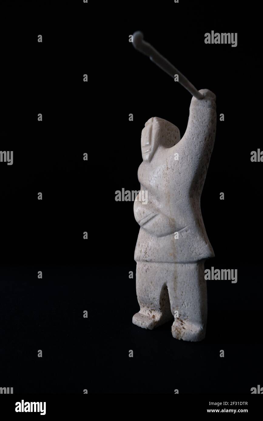Petite statue de chasseur inuit avec une lance en os animal. Isolé sur fond noir. Art inuit. Culture tribale des indigènes dans le nord Banque D'Images