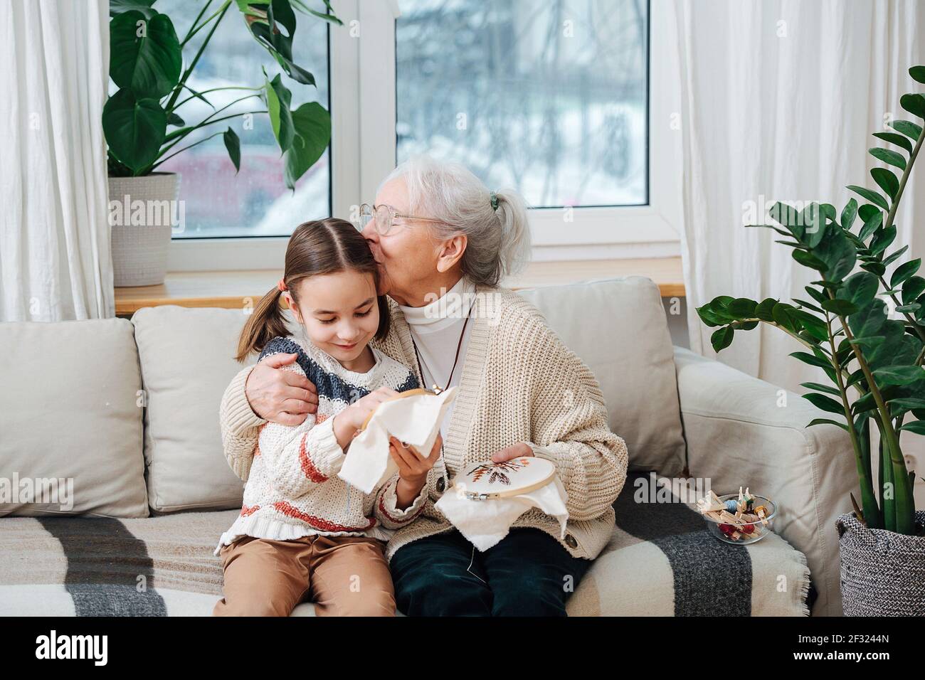 Affectueux et assis sur un canapé avec sa petite-fille, ils brodaient ensemble une boucle. Elle est fière d'elle, embrassant ses cheveux. Banque D'Images