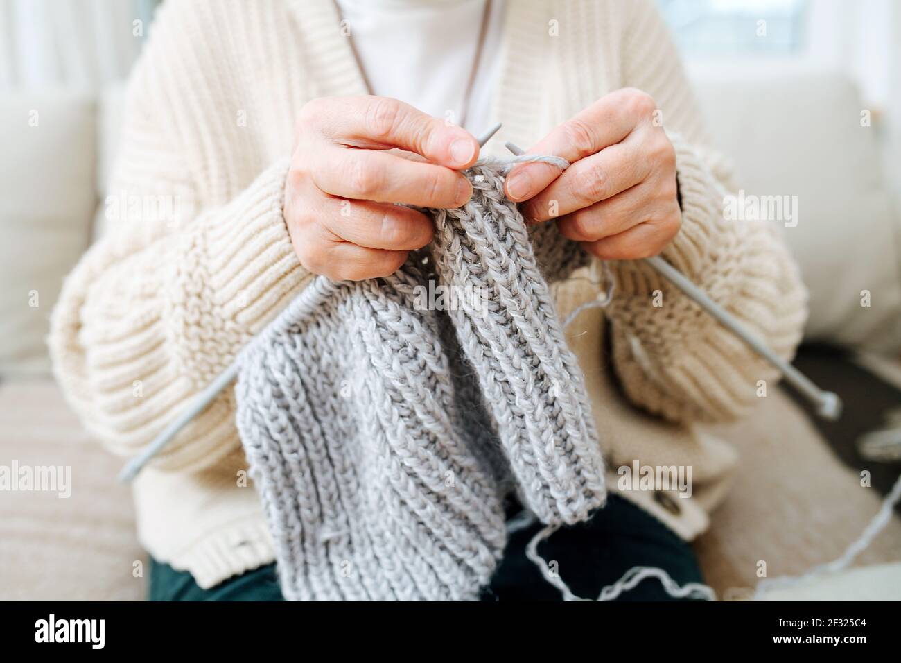 Granny assis sur un canapé à la maison, tricotage avec des aiguilles, avec de la laine grise. Rogné, pas de visage. Banque D'Images