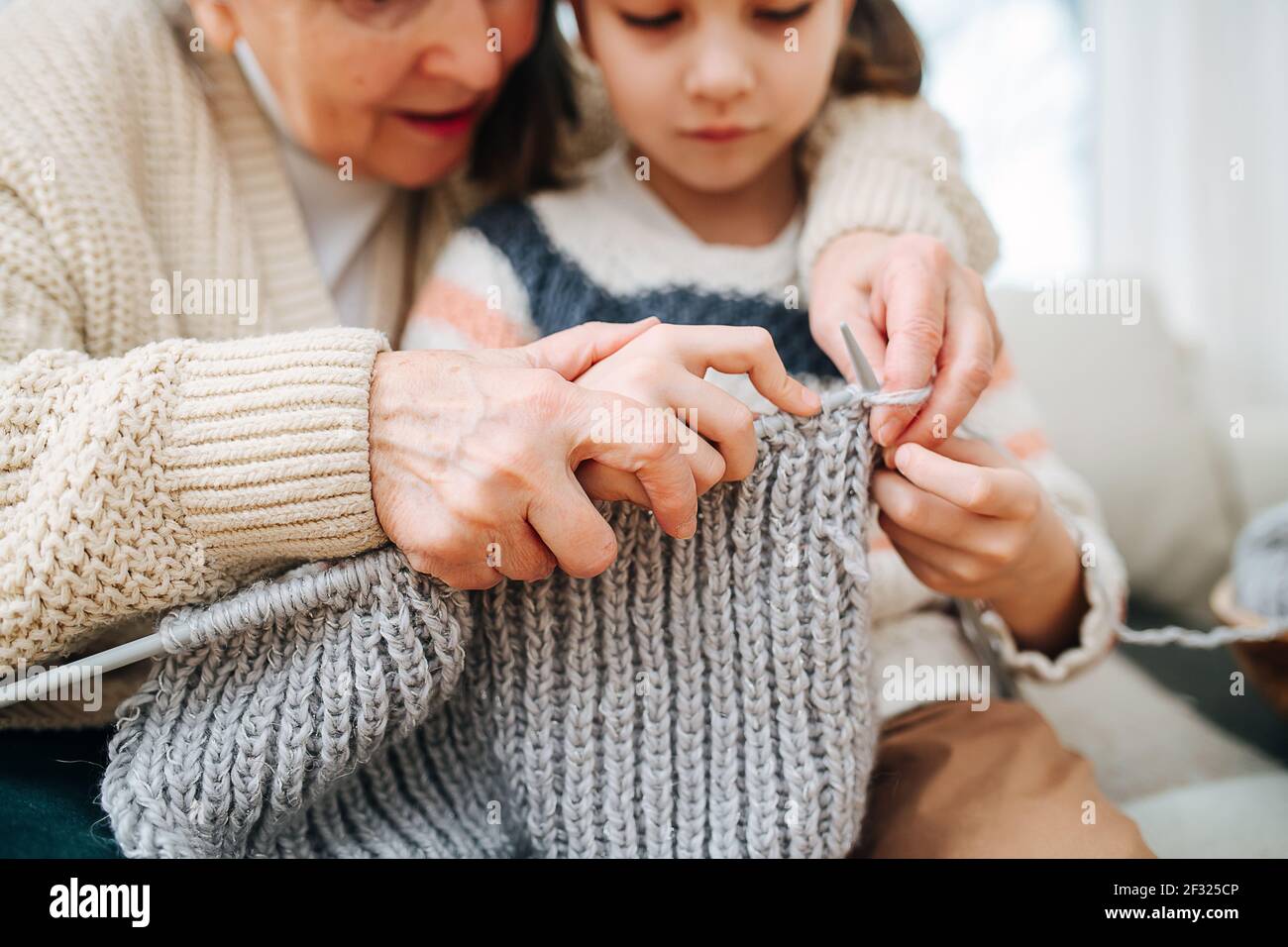 Une grande granny enthousiaste assise sur un canapé avec sa petite-fille, elle lui apprend à tricoter, en tenant les mains au-dessus de ses arrières. Gros plan, concentrez-vous sur vos mains. Faces Banque D'Images