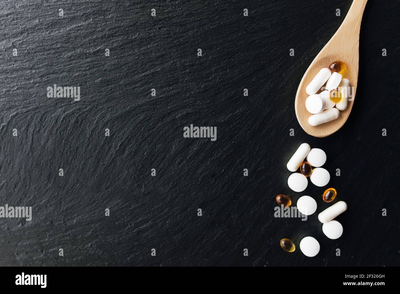 Poser à plat avec oméga 3 et capsules de vitamine sur une cuillère en bois sur fond de béton noir. Concept de santé. Pilules de vitamines. Photo de haute qualité Banque D'Images