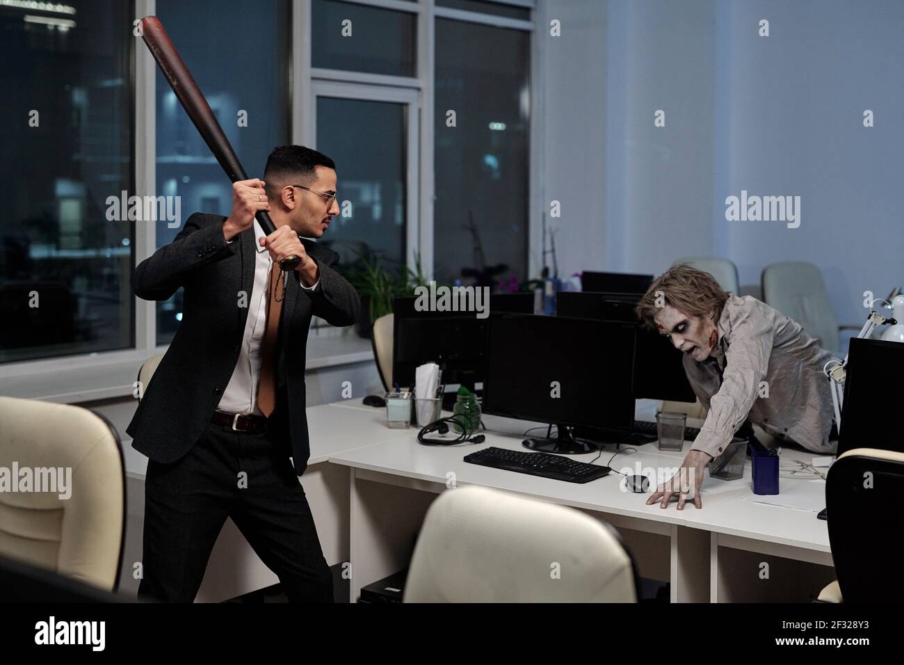 Un jeune homme d'affaires en colère avec une batte de baseball qui va frapper effrayé homme avec zombie greasepaint sur son visage et les mains essayant pour se mettre à la réception Banque D'Images