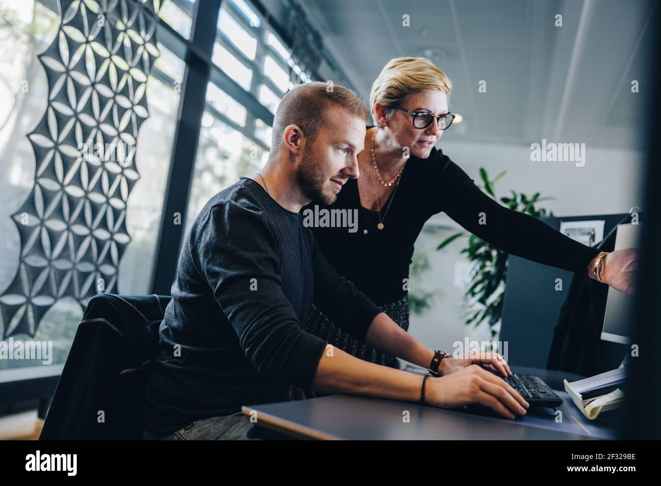 Femme d'affaires senior pointant sur un moniteur d'ordinateur et discutant du travail avec un collègue assis à son bureau. Deux professionnels travaillant ensemble Banque D'Images