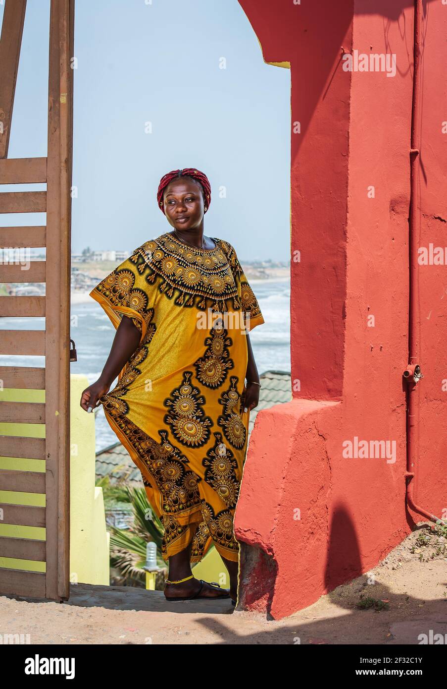 Femme africaine portant un costume jaune se tient à une porte avec Contexte de la ville d'Accra au Ghana Banque D'Images