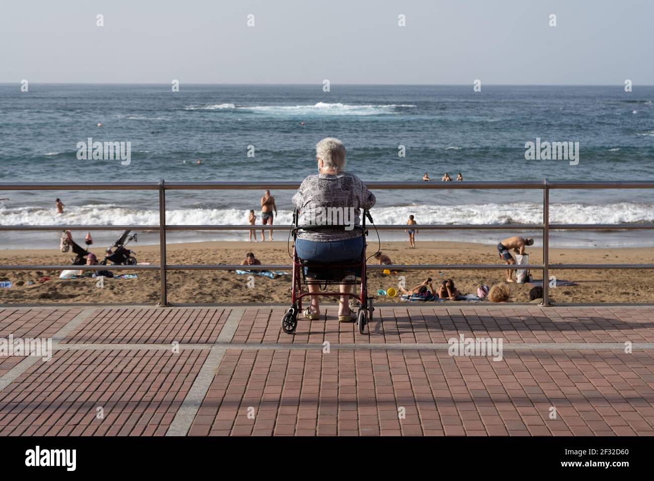 Plage de Las Canteras à Las Palmas de Gran Canaria, Espagne - 19 février 2021 : une femme âgée assise dans son cadre de marche et regardant les gens se baigner sur la Banque D'Images