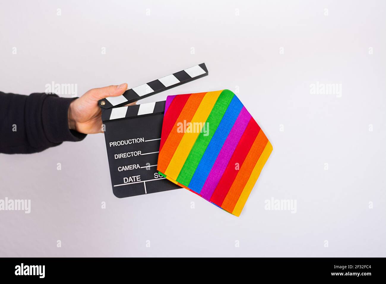 Main d'un homme tenant un drapeau arc-en-ciel LGBT et un film carte clapper Banque D'Images