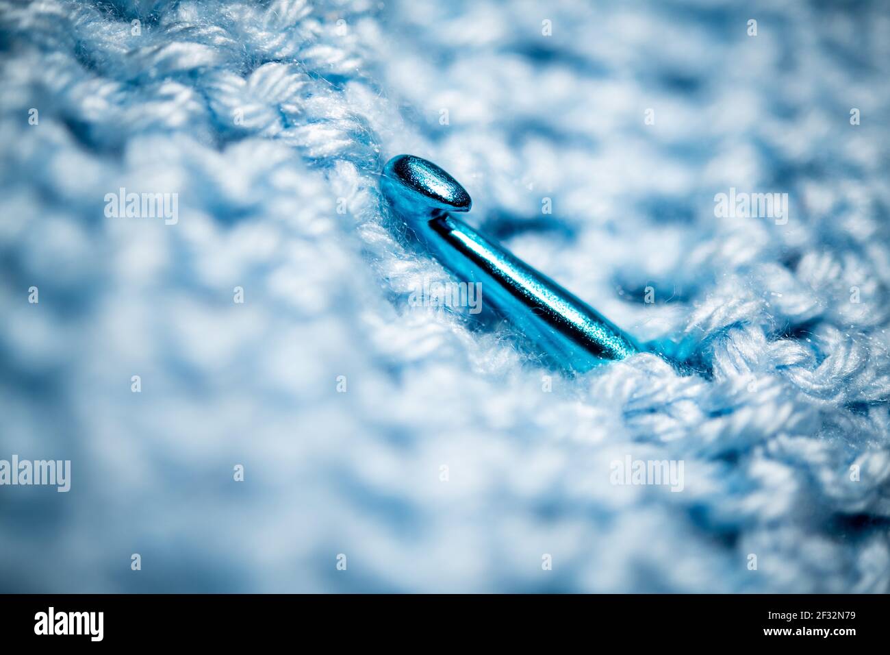 Un gros plan extrême avec mise au point sélective d'un morceau de tissu bleu foncé en crochet avec aiguille bleue en crochet. Banque D'Images