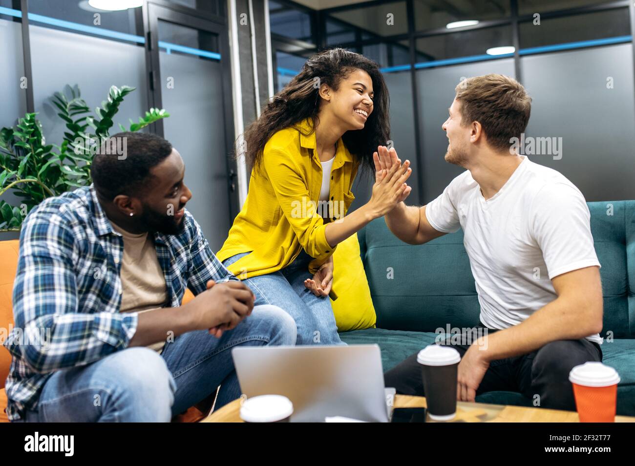 Des étudiants multiraciaux satisfaits ou des collègues assis dans un bureau moderne, bien fait avec le projet d'entreprise. Des collègues qui ont réussi à se donner des cinq hauts, souriant, heureux au sujet du bon travail Banque D'Images