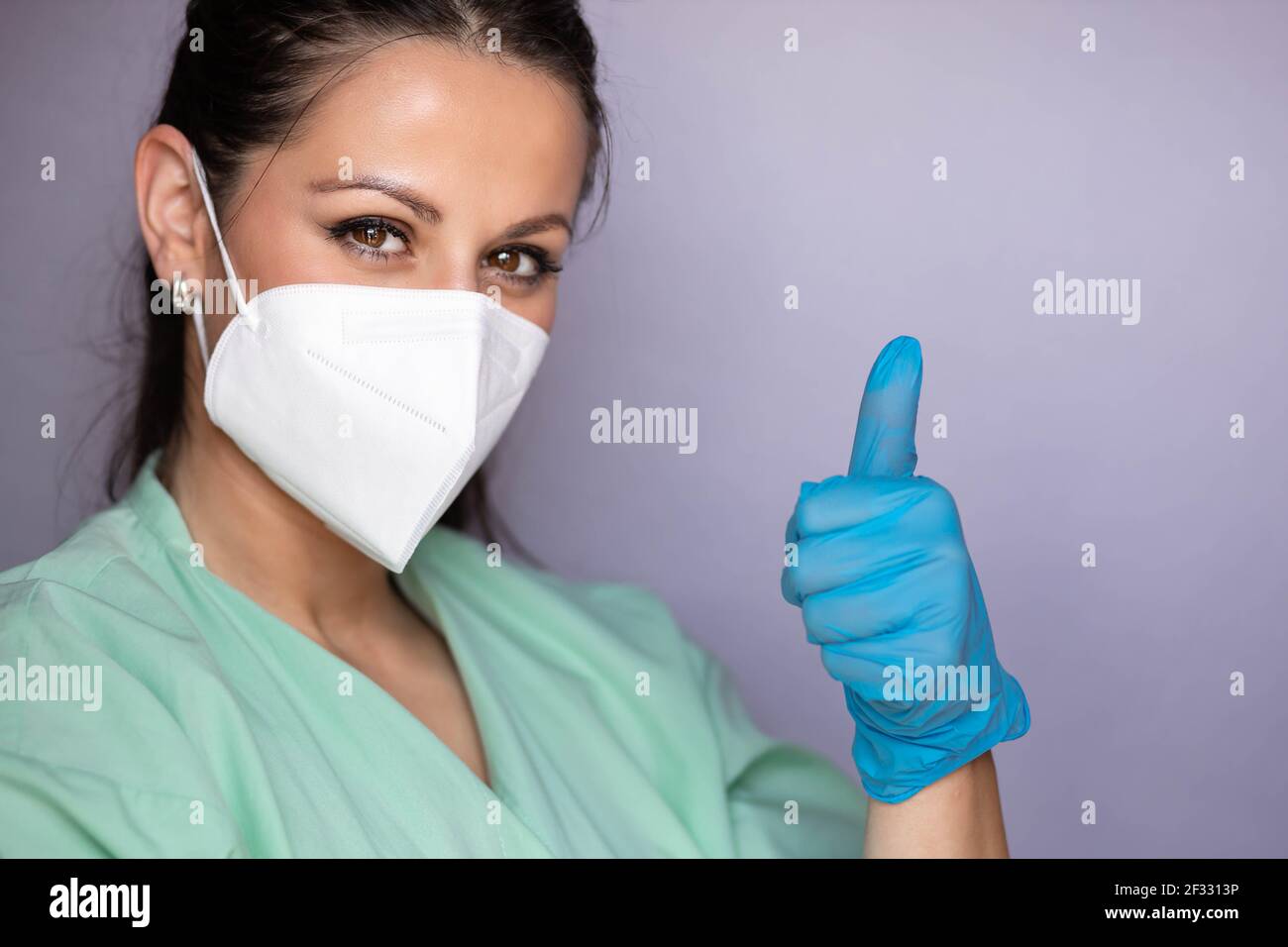 Jeune professionnel de la santé, l'infirmière avec un masque de protection et des yeux souriants, montrant le pouce vers le haut. Isolé sur fond gris Banque D'Images