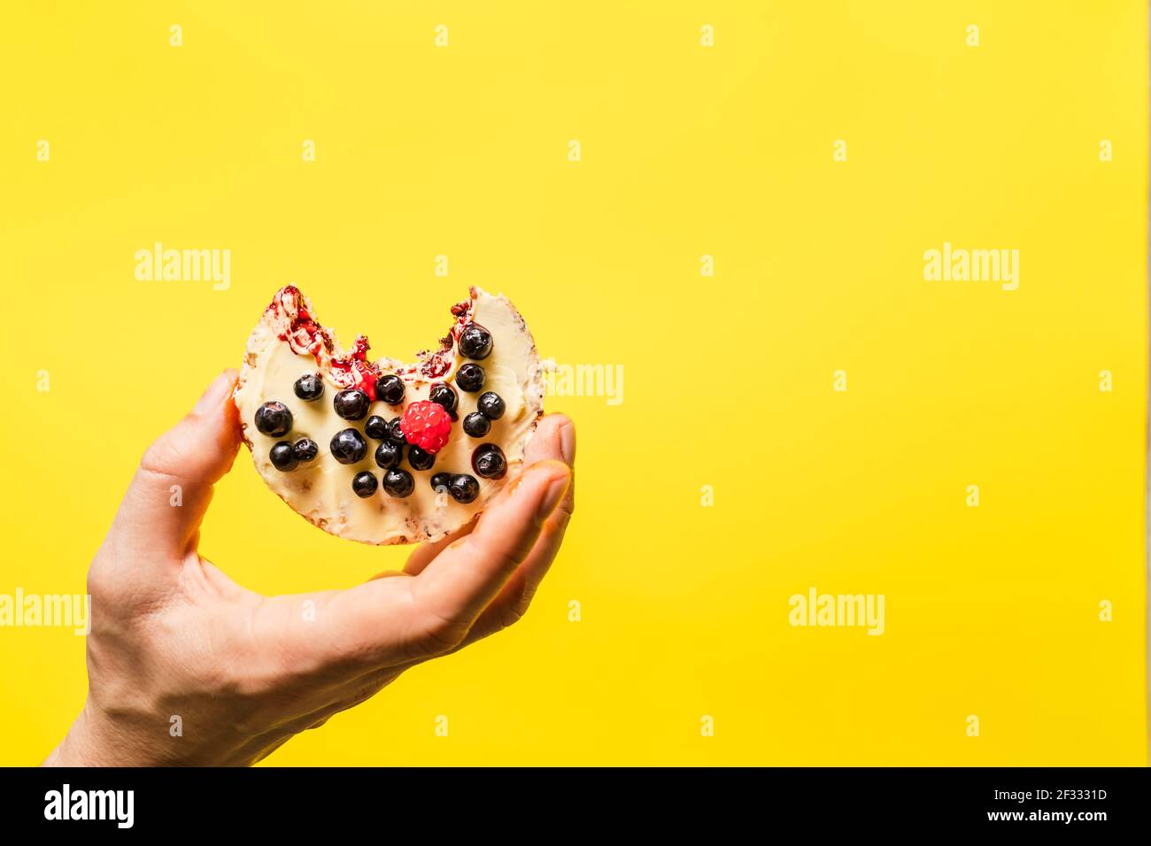 Main tenant un gâteau de riz soufflé croustillant aux bleuets de fruits frais framboises en face du fond jaune - sain végétarien biologique ou ve Banque D'Images