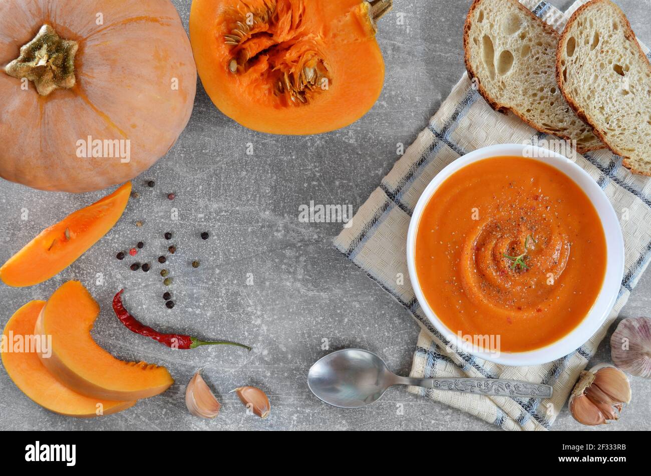 Soupe de potiron piquant dans un bol blanc à côté de potiron frais, tranches de pain et épices sur fond gris, plat. Concept de saine alimentation. Banque D'Images