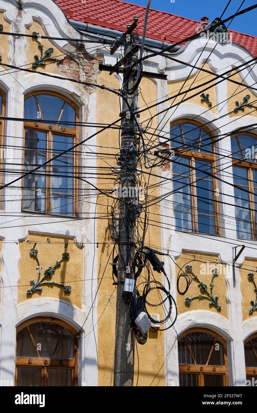 Enchevêtrement de fils électriques sur le poteau contre le bâtiment traditionnel. Réseau complexe d'au-dessus du sol en Roumanie Banque D'Images