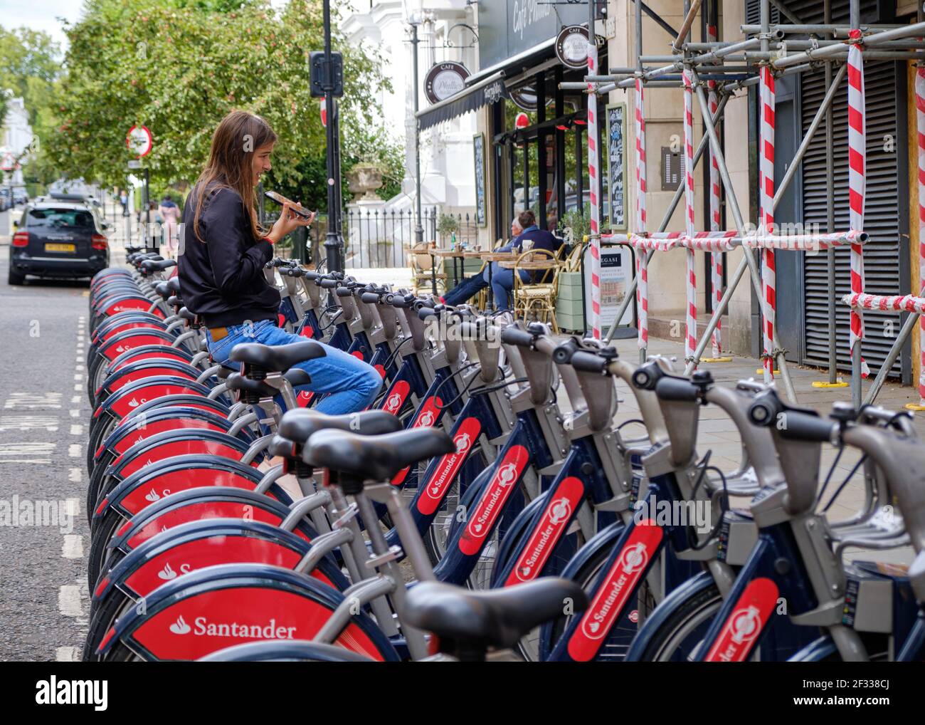 Santander vélo station complètement chargée, avec une femme utilisant un vélo comme siège pendant qu'elle parle au téléphone à Londres Banque D'Images