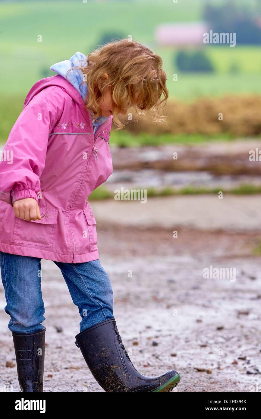 Pleine fille de corps en imperméable rose et bottes en caoutchouc jouant dans la flaque de boue dans la campagne Banque D'Images