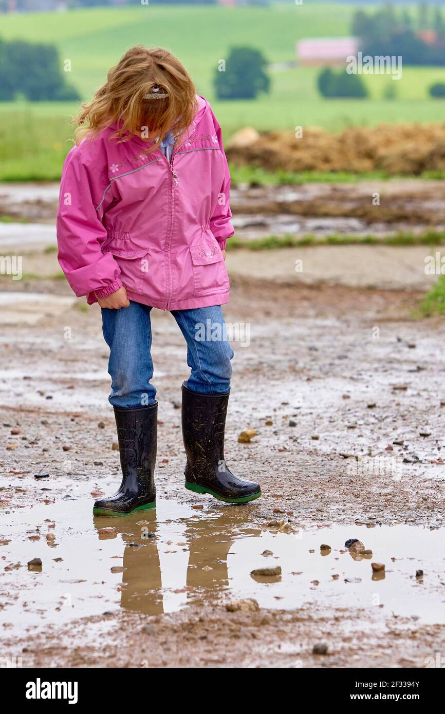 Pleine fille de corps en imperméable rose et bottes en caoutchouc jouant dans la flaque de boue dans la campagne Banque D'Images