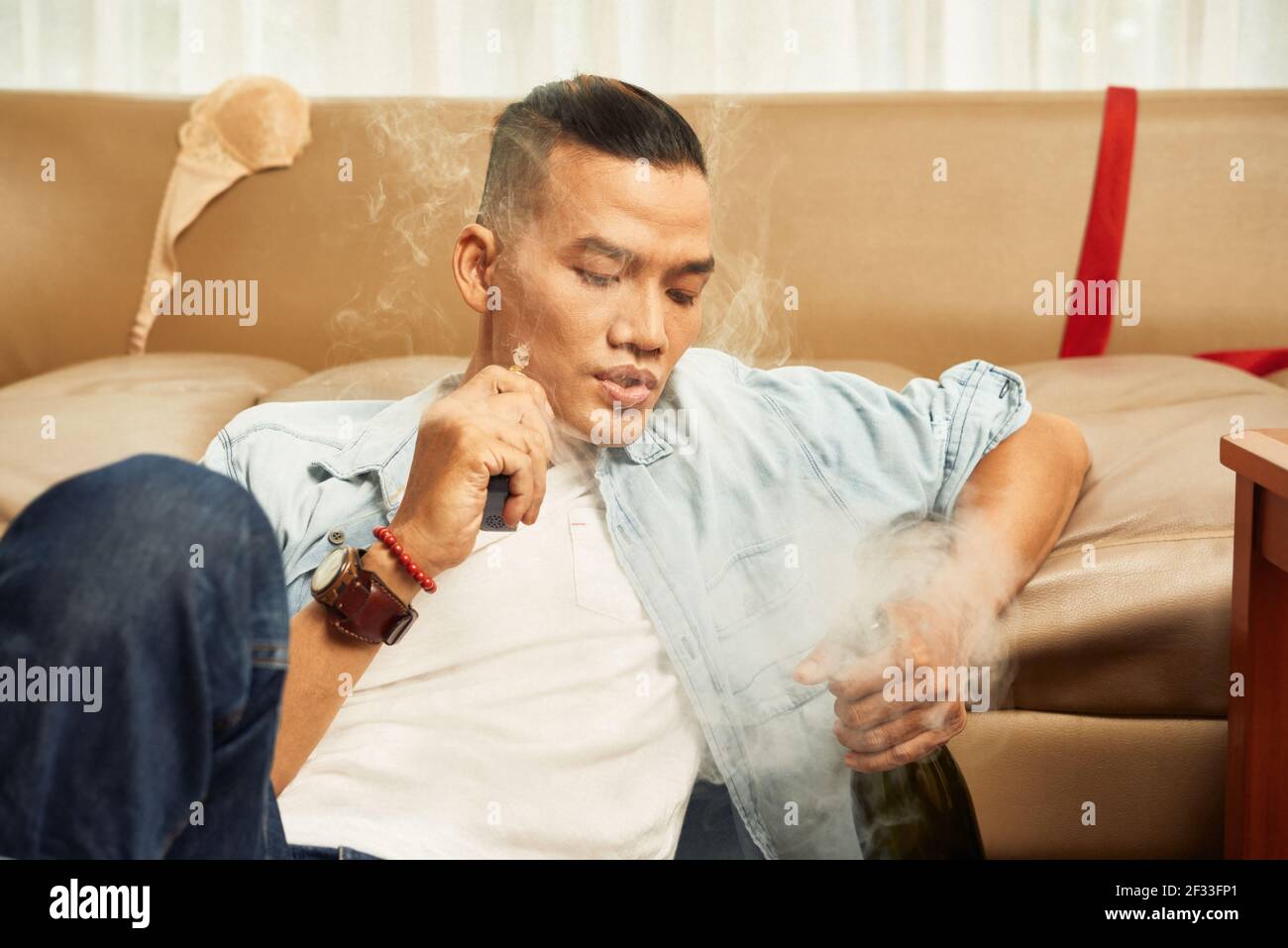 Beau jeune homme asiatique fumant de la cigarette et buvant de l'alcool à accueil Banque D'Images