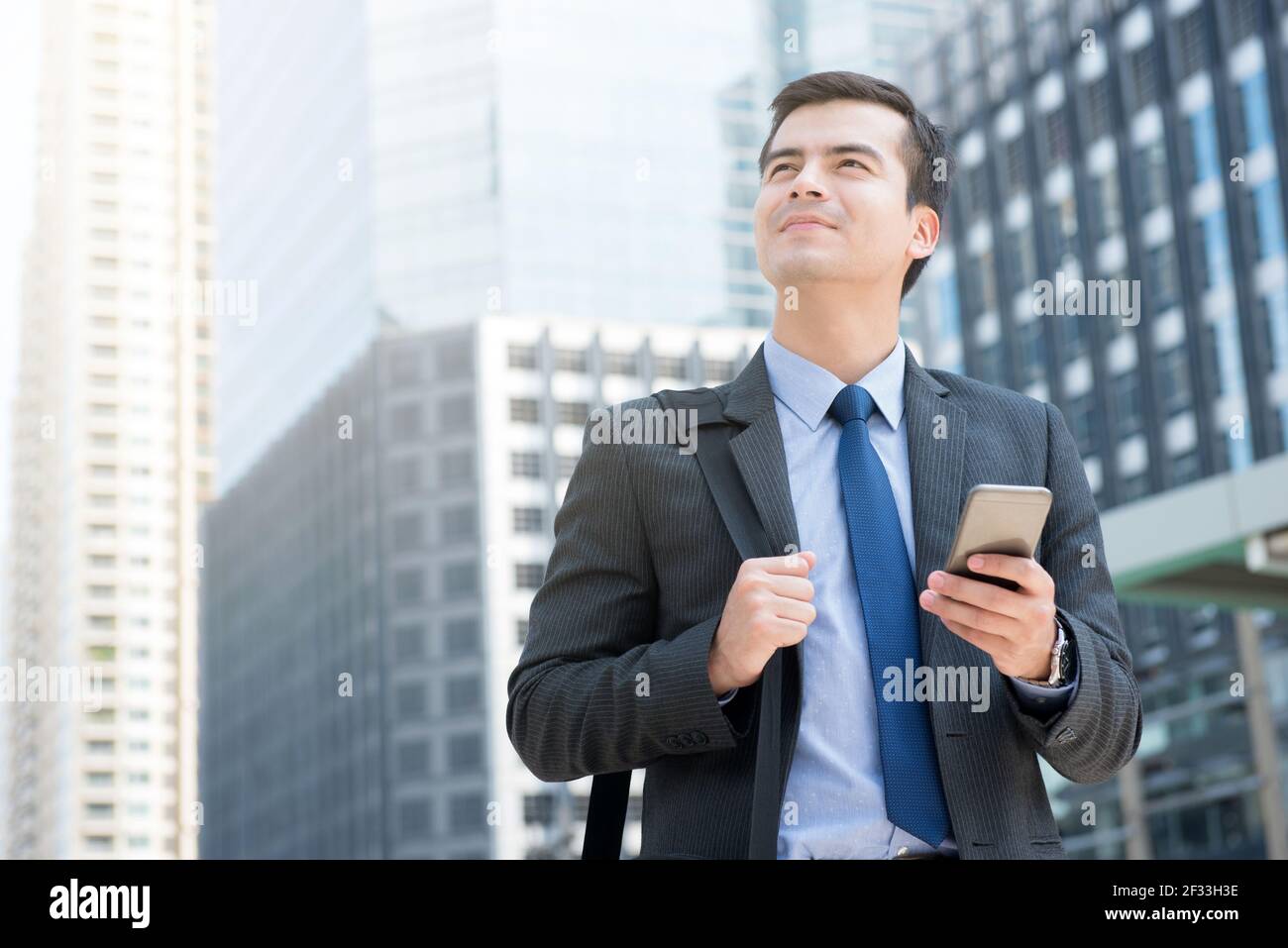 Jeune homme d'affaires utilisant un téléphone portable tout en portant la sacoche dans le ville : voyages d'affaires et roaming mobile Banque D'Images