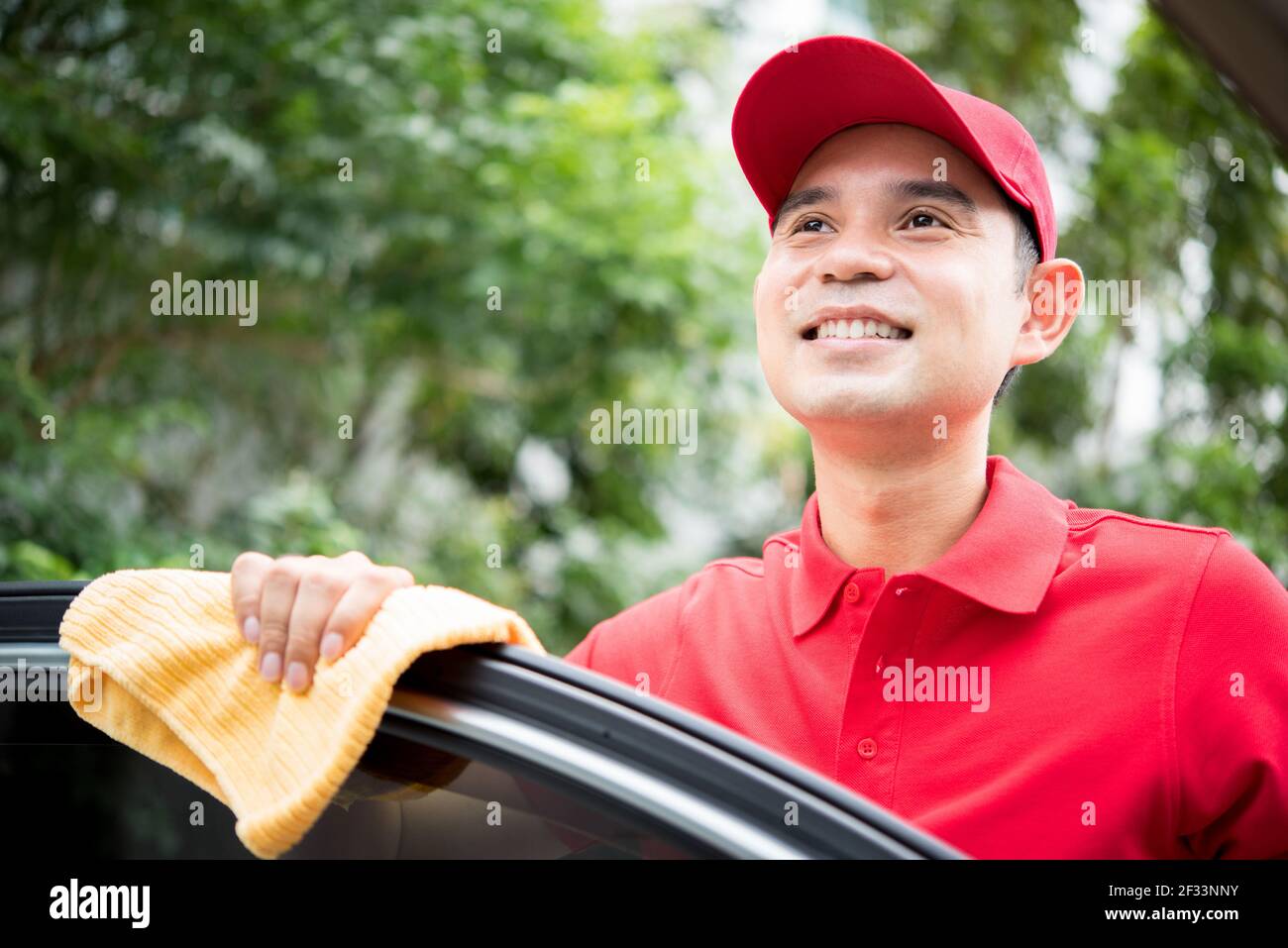 Le personnel souriant du service automobile pense (rêvant de la journée) lors du nettoyage de la porte de la voiture Banque D'Images