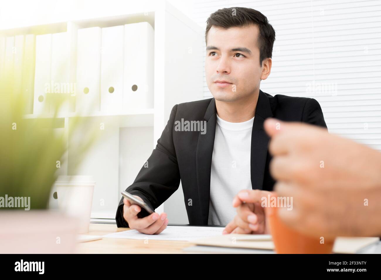 Jeune homme d'affaires élégant tenant un smartphone tout en étant assis dans le bureau Banque D'Images