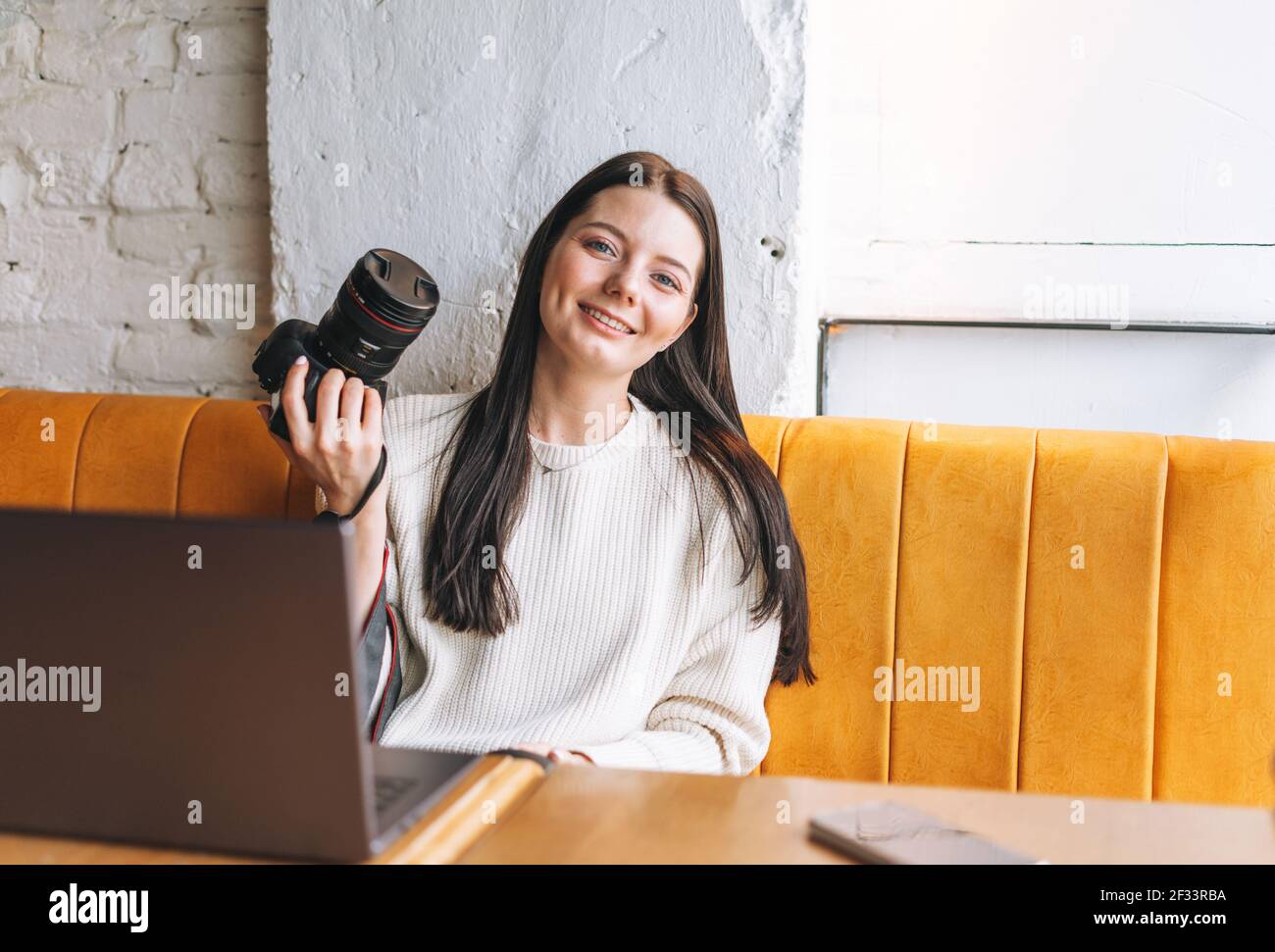 Brunette jeune femme souriante photographe travaillant avec son appareil photo et ordinateur portable dans le café Banque D'Images