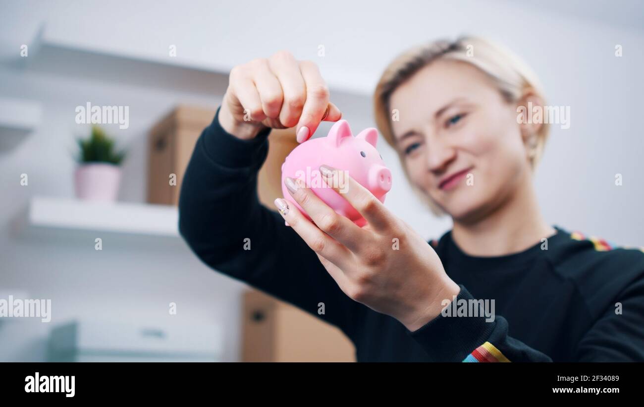 Portrait d'une jeune femme caucasienne heureuse mettant des pièces de monnaie dans la banque de piggy. Photo de haute qualité Banque D'Images