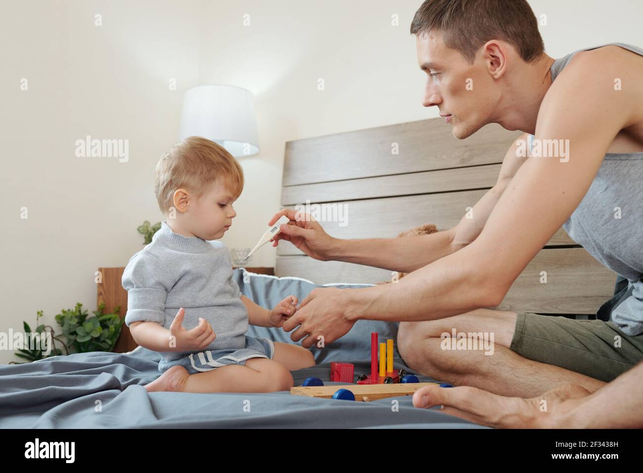Petit garçon assis sur le lit et jouant pendant que son père mesure de sa  température pendant la maladie Photo Stock - Alamy